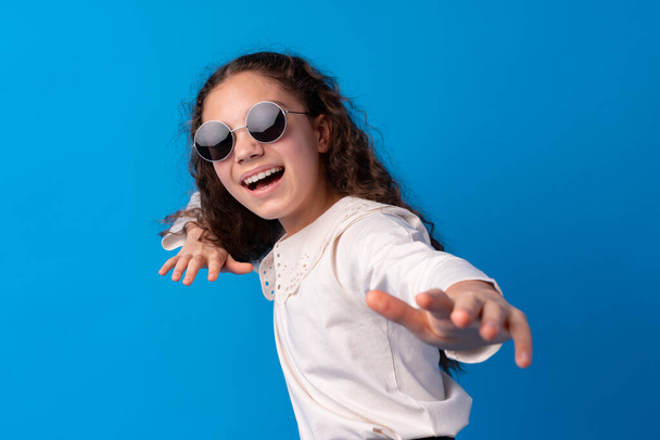 Little fashion girl in sunglasses against blue background - Foto, immagini