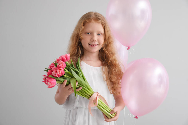 Kleines rothaariges Mädchen mit Tulpen und Luftballons auf hellem Hintergrund. Internationaler Frauentag - Foto, Bild