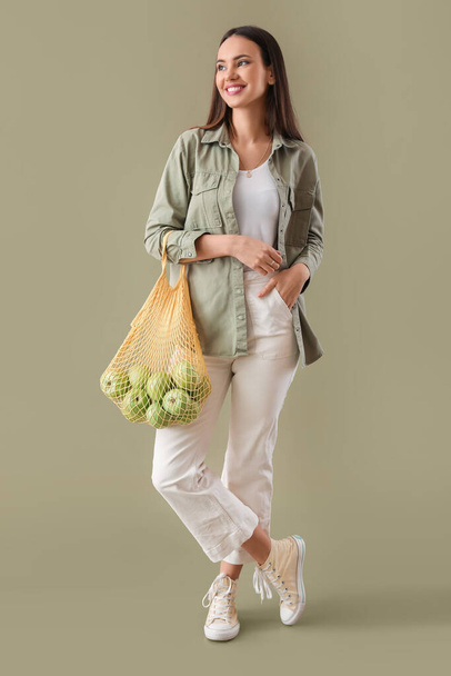 Young woman holding string bag with apples on color background - Foto, imagen