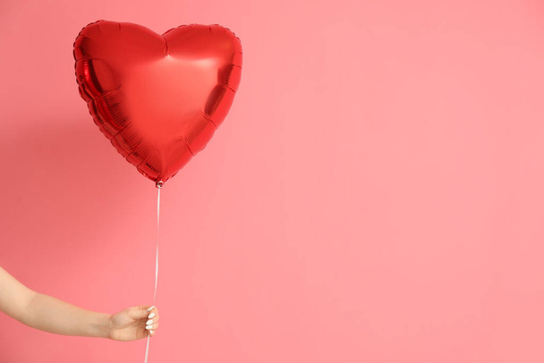 Female hand with beautiful heart-shaped balloon for Valentine's Day celebration on pink background - Fotoğraf, Görsel