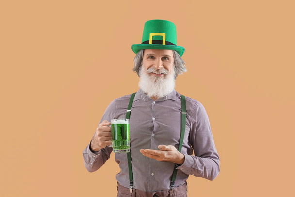 Starszy pan w zielonym kapeluszu ze szklanką piwa na beżowym tle. Święto św. Patryka - Zdjęcie, obraz