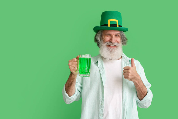 Старший чоловік у капелюсі зі склянкою пива показує пальцем на зеленому фоні. День святого Патрика. - Фото, зображення