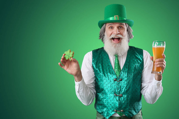 Surprised senior man with cookie and glass of beer on green background. St. Patrick's Day celebration - 写真・画像