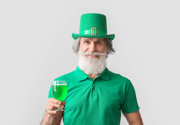 Homme âgé en chapeau vert avec de la bière sur fond clair. Célébration de la Saint Patrick - Photo, image