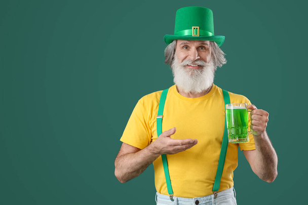 Senior man met een glas bier op groene achtergrond. St. Patrick 's Day viering - Foto, afbeelding