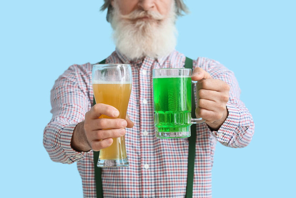 青い背景にビールのグラスを持つシニア男性、クローズアップ。聖パトリックの日のお祝い - 写真・画像