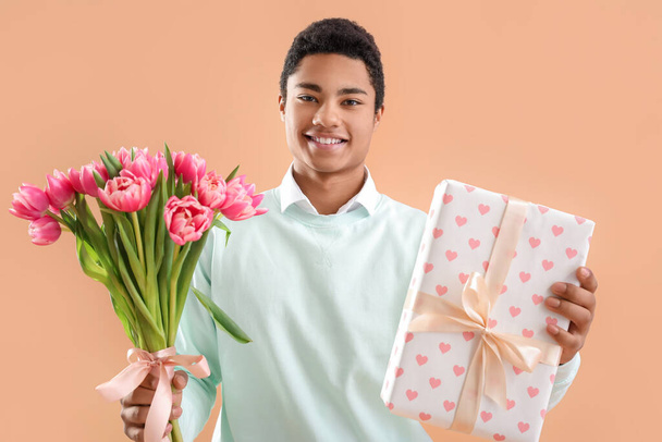 African-American man with gift box and bouquet of flowers on color background. International Women's Day celebration - Foto, immagini