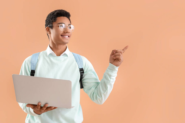 Studente afro-americano maschio con computer portatile moderno che punta a qualcosa sullo sfondo di colore - Foto, immagini