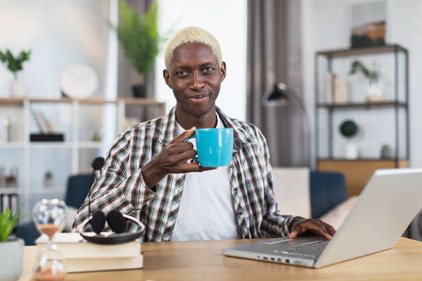 African american young sitting at desk with tea and laptop - Fotografie, Obrázek