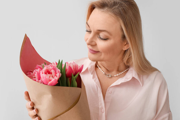 Woman with bouquet of tulips on light background. International Women's Day celebration - Photo, Image