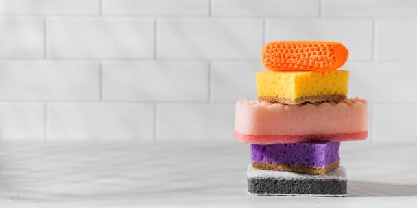 Multicolored sponges for washing dishes are stacked on a white tiled background. - Foto, Bild