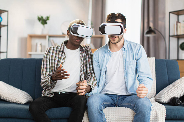 Multicultural gay couple in VR headset sitting on couch - Fotoğraf, Görsel