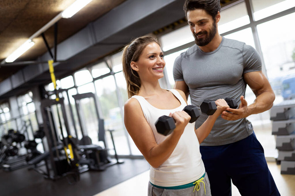 Fit happy woman with her personal fitness trainer in the gym exercising with dumbbells. Sport people workout concept - Zdjęcie, obraz