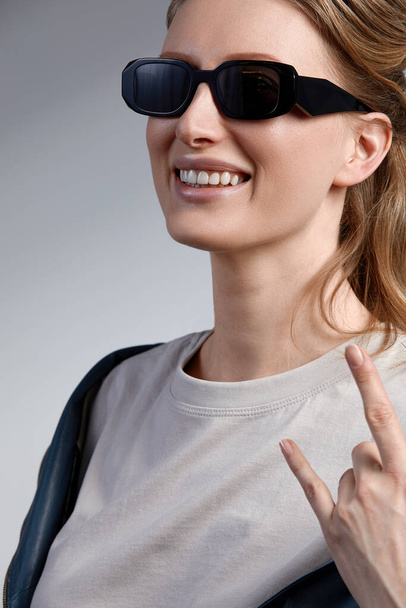 Улыбающаяся модель в модных солнцезащитных очках с камнем на пальцах. Портрет крупного плана - Фото, изображение