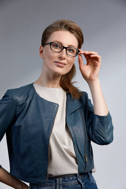 Красивая молодая кавказская студия бизнесвумен снималась на сером фоне. Очаровательная и уверенная в себе серьезная блондинка в тёмно-синем пиджаке в очках - Фото, изображение