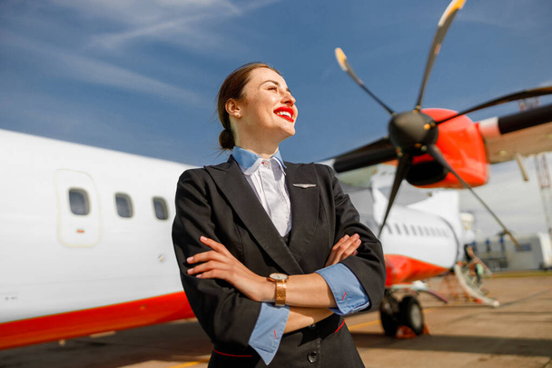 Iloinen nainen lentoemäntä seisoo lähellä lentokonetta lentokentällä - Valokuva, kuva