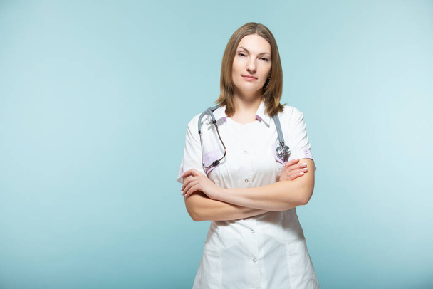 Beautiful female doctor with a stethoscope with crossed arms on a blue background. healthcare concept. - 写真・画像