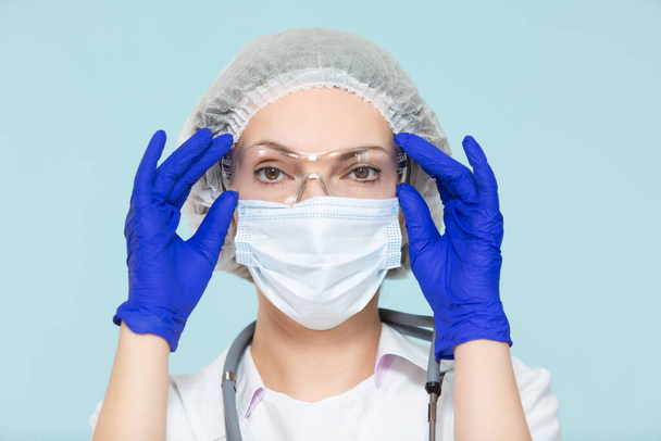 Doctor or nurse woman in a personal protective suit with a stethoscope, on a blue background. In a mask, gloves, goggles and a hat. Copy paste. healthcare concept. - Foto, Imagen