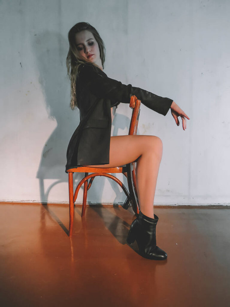 Attractive young blonde woman in black underwear with a slim figure and beautiful legs in boots posing on a chair against the wall, aesthetics and beauty,body care, fashion and style - Φωτογραφία, εικόνα