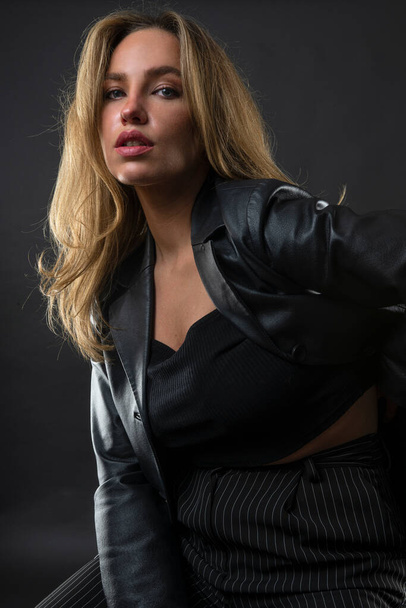 Porträt einer schönen blonden Frau in schwarzer Jacke und weißem Hemd auf dunklem Hintergrund - Foto, Bild