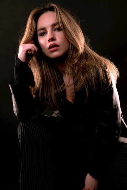 beautiful young woman with long hair in black dress posing on dark background - Фото, зображення