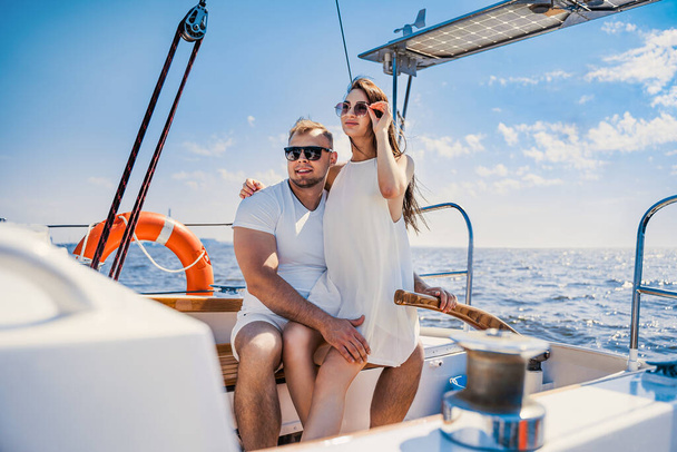 happy young couple in white clothing sitting together on yacht while looking at the blue sea - Fotoğraf, Görsel