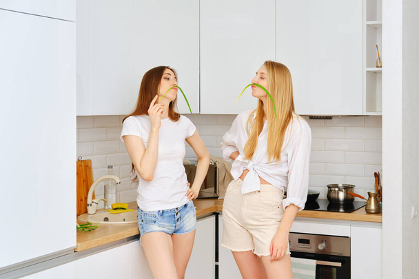 Two funny women playing with onion in the kitchen, having fun and make faces. - 写真・画像