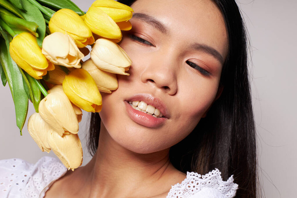 Charming young Asian woman with a bouquet of flowers smile close-up light background unaltered - Valokuva, kuva