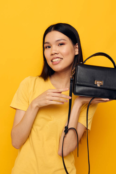 funny asian woman in a yellow t-shirt black womens bag in hands posing - Valokuva, kuva