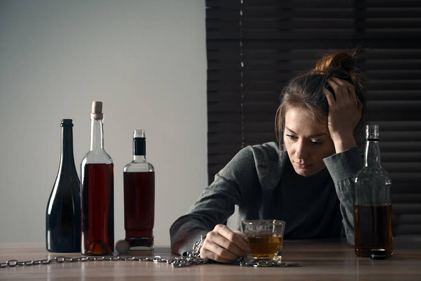 Adicción al alcohol. Mujer encadenada con vaso de licor en la mesa de madera en la habitación - Foto, imagen