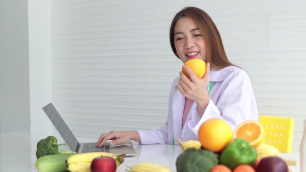 Asiatische Ärztin oder Ernährungsberaterin. Auf dem weißen Tisch lagen verschiedene Obst- und Gemüsesorten. Gesundheitskonzepte, gesunde Ernährung, Gewichtsverlust - Filmmaterial, Video