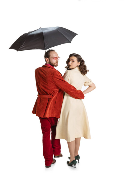 Young family couple, man and woman in retro style bright clothes, fashion of 70s, 60s years walking with umbrella isolated on white studio background - Zdjęcie, obraz