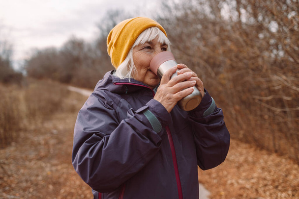 Viajante anciana sosteniendo taza de termo en el viajero de la ciudad en la hermosa naturaleza. Concepto ecológico de cero residuos - Foto, Imagen
