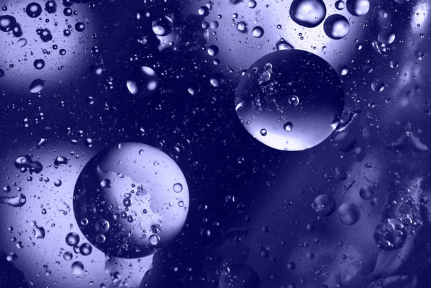 Primer plano de gotas de aceite y aire y burbujas en la superficie del agua líquida. Fondo abstracto con círculos tonificados en muy peri, color del año 2022. Copiar espacio. Directamente encima de la vista. Orientación horizontal. - Foto, Imagen