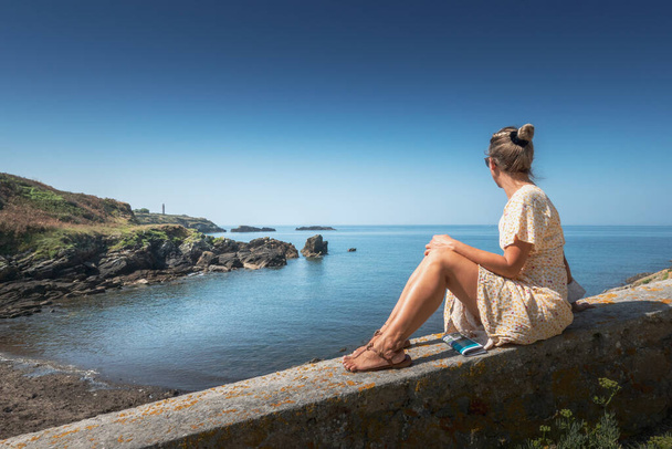 Женщина, сидящая на набережной с видом на море, Бретань, Франция - Фото, изображение