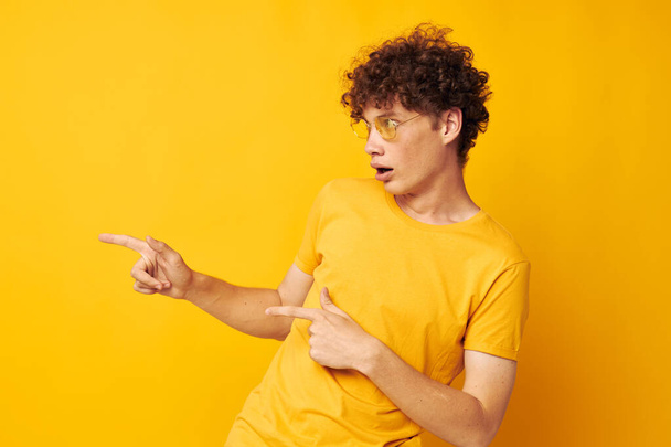 portrait of a young curly man wearing stylish glasses yellow t-shirt posing Lifestyle unaltered - Foto, imagen