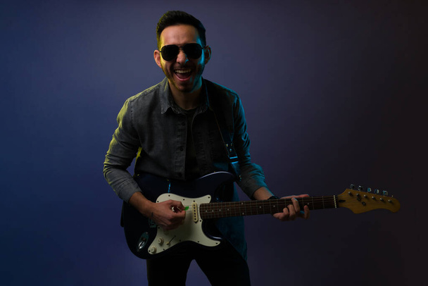 Обожаю хард-рок! Счастливый мужчина-музыкант, играющий на электрогитаре и взволнованный во время концерта - Фото, изображение