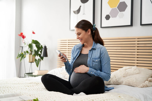 Femme caucasienne en grossesse avancée en utilisant un téléphone mobile à la maison - Photo, image