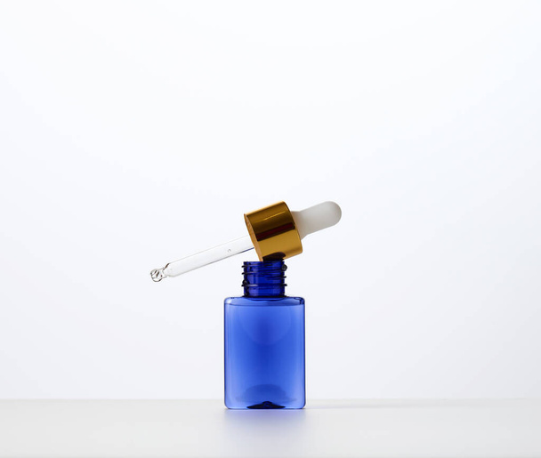 botella de vidrio azul con una pipeta sobre un fondo blanco. Plantilla para productos cosméticos líquidos, publicidad y promoción - Foto, imagen