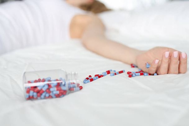 Dode vrouw liggend op bed met verspreide medische capsules close-up - Foto, afbeelding