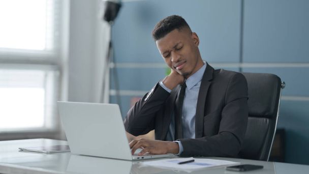 Afrikanischer Geschäftsmann hat Nackenschmerzen, während er Laptop im Büro benutzt - Foto, Bild