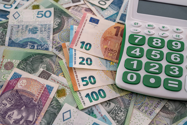 zeer grote hoeveelheden eurobankbiljetten en Poolse nieuwe zloty 's en een rekenmachine met een prachtig toetsenbord. Bedrijfsconcept - Foto, afbeelding