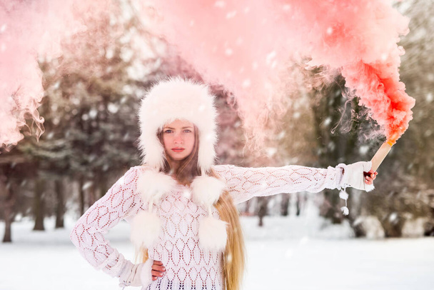 jong mooi meisje met rood gekleurde rook bom in de hand in de winter dag. - Foto, afbeelding
