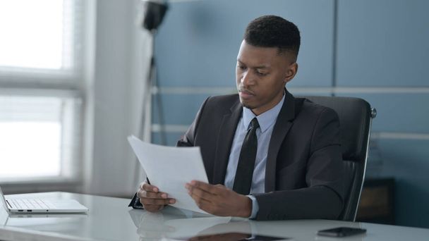 Αφρικανός επιχειρηματίας Διαβάζοντας εκθέσεις, ενώ κάθεται στο γραφείο - Φωτογραφία, εικόνα