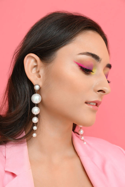 Woman with creative makeup and stylish earrings on pink background. International Women's Day - Фото, зображення