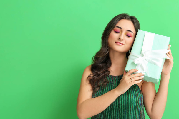 Woman with creative makeup holding gift box on green background. International Women's Day - Fotoğraf, Görsel