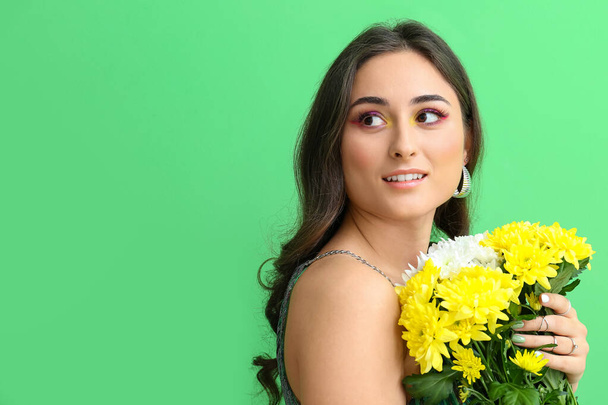 Женщина с креативным макияжем держит букет цветов и смотрит в сторону на зеленом фоне. Международный женский день - Фото, изображение