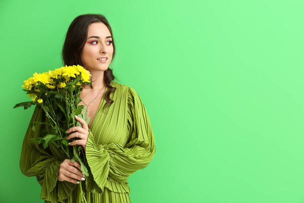 Young woman with creative makeup holding bouquet of flowers and looking aside on green background. International Women's Day - Foto, Imagem