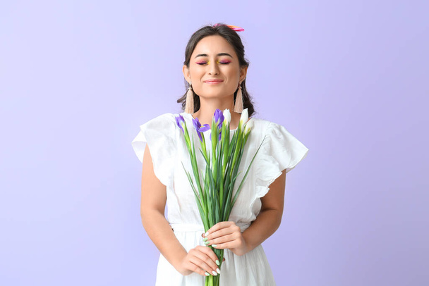 Femme avec un maquillage créatif et les yeux fermés tenant fleurs d'iris sur fond violet. Journée internationale de la femme - Photo, image