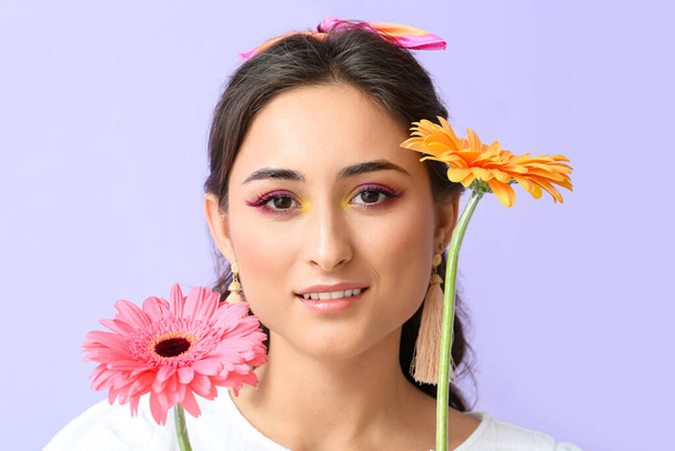 Yaratıcı makyajı ve mor arka planda Gerbera çiçekleri olan genç bir kadının portresi. Uluslararası Kadınlar Günü - Fotoğraf, Görsel